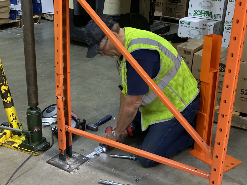 Rack repair specialist is cutting the anchor bolts underneath the pallet rack base-plate using a saws-all.